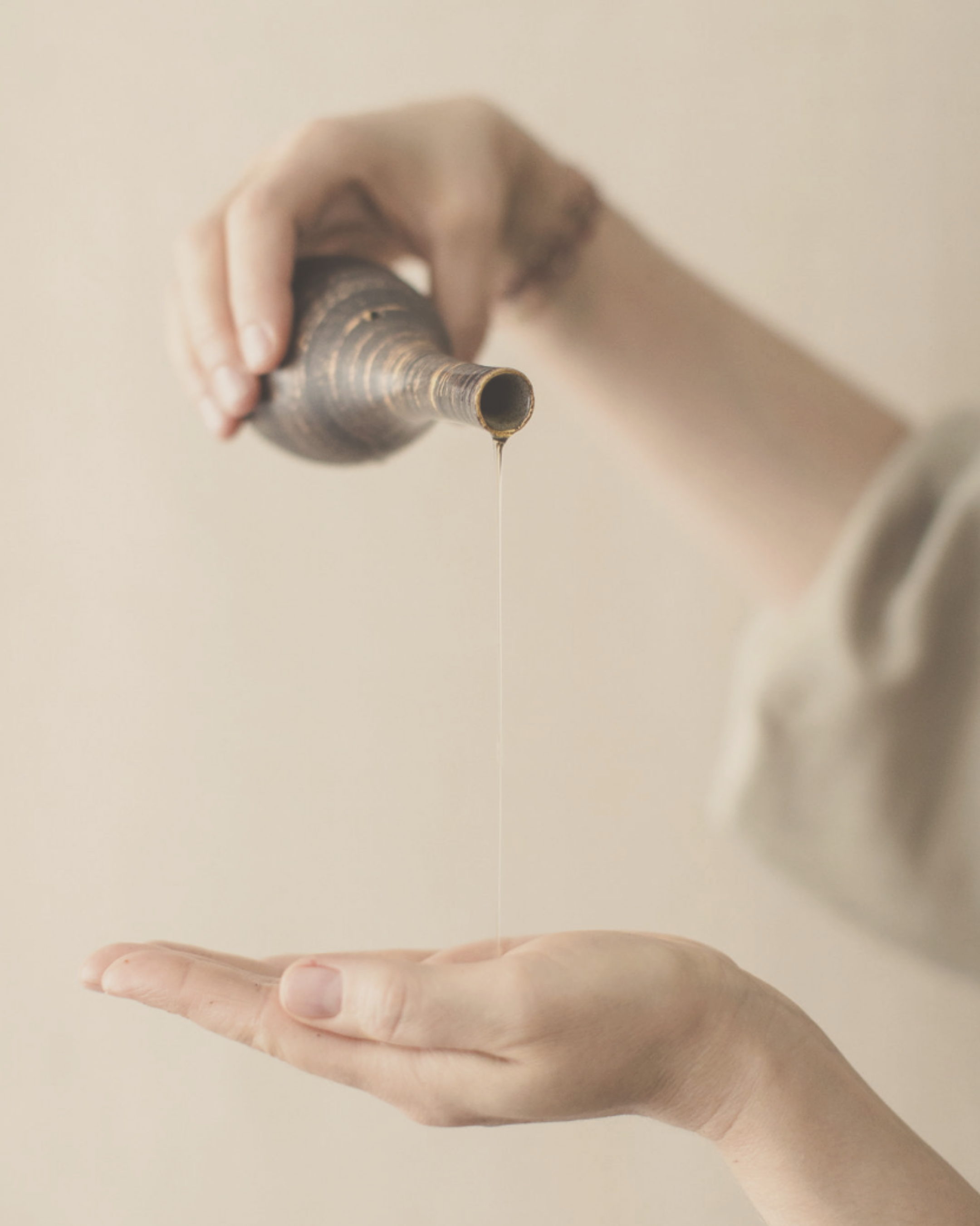 woman pouring medical Ayurvedic oil into her hand from a copper carafe 