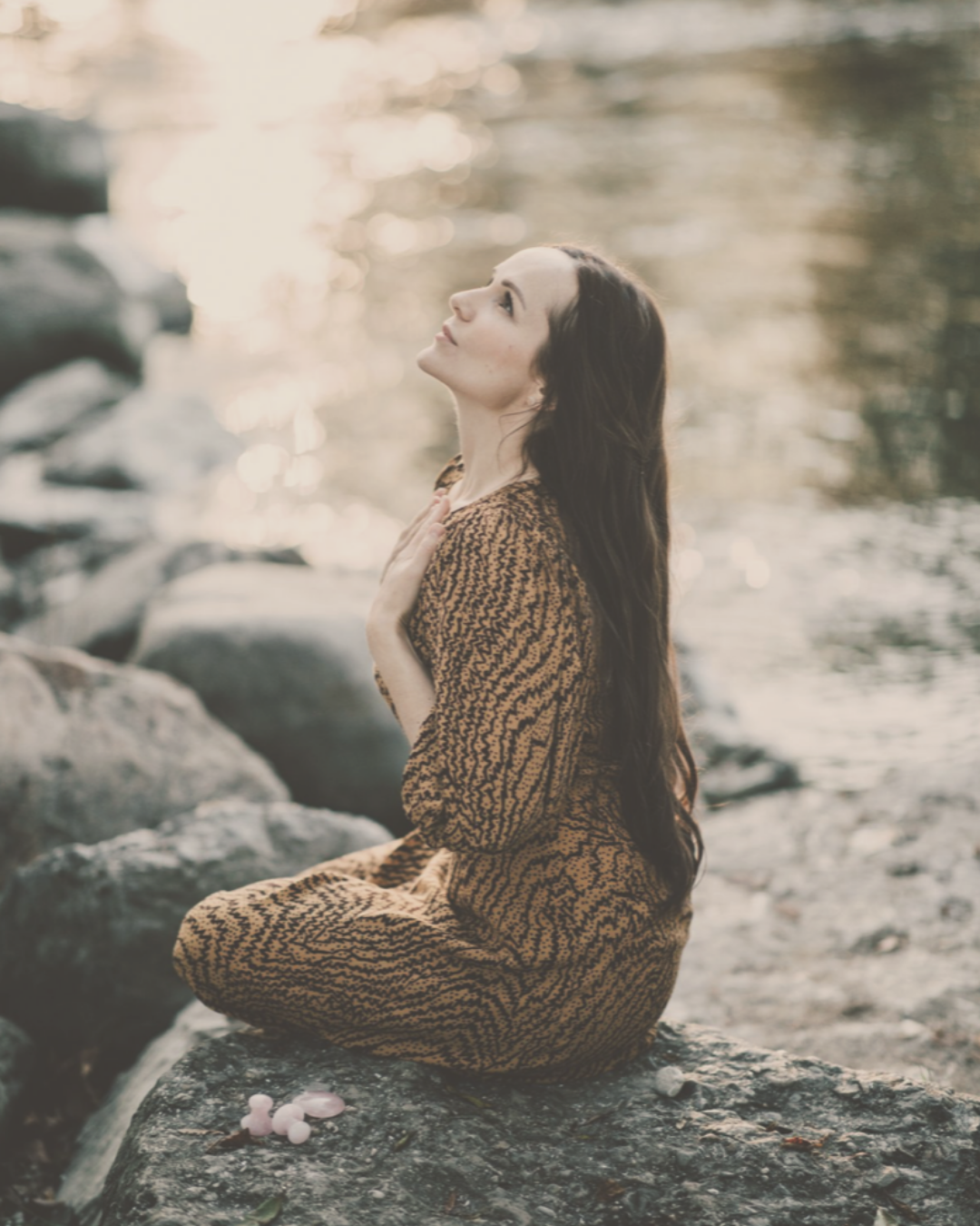 woman sitting at the river in a late summer afternoon holding her hand to her heart looking up to the sky immersed into the golden light of the sun