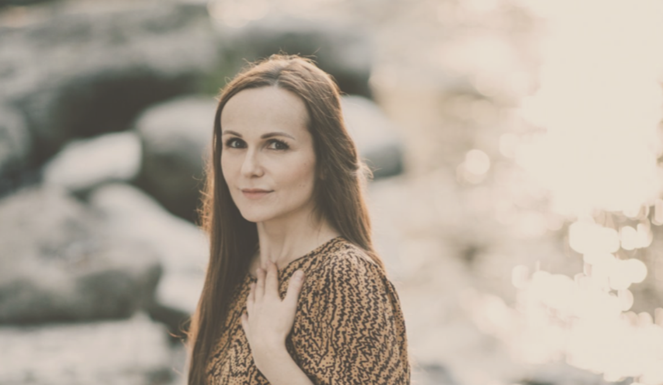 woman sitting at the river in a late summer afternoon holding her hand to her heart immersed into the golden light of the sun