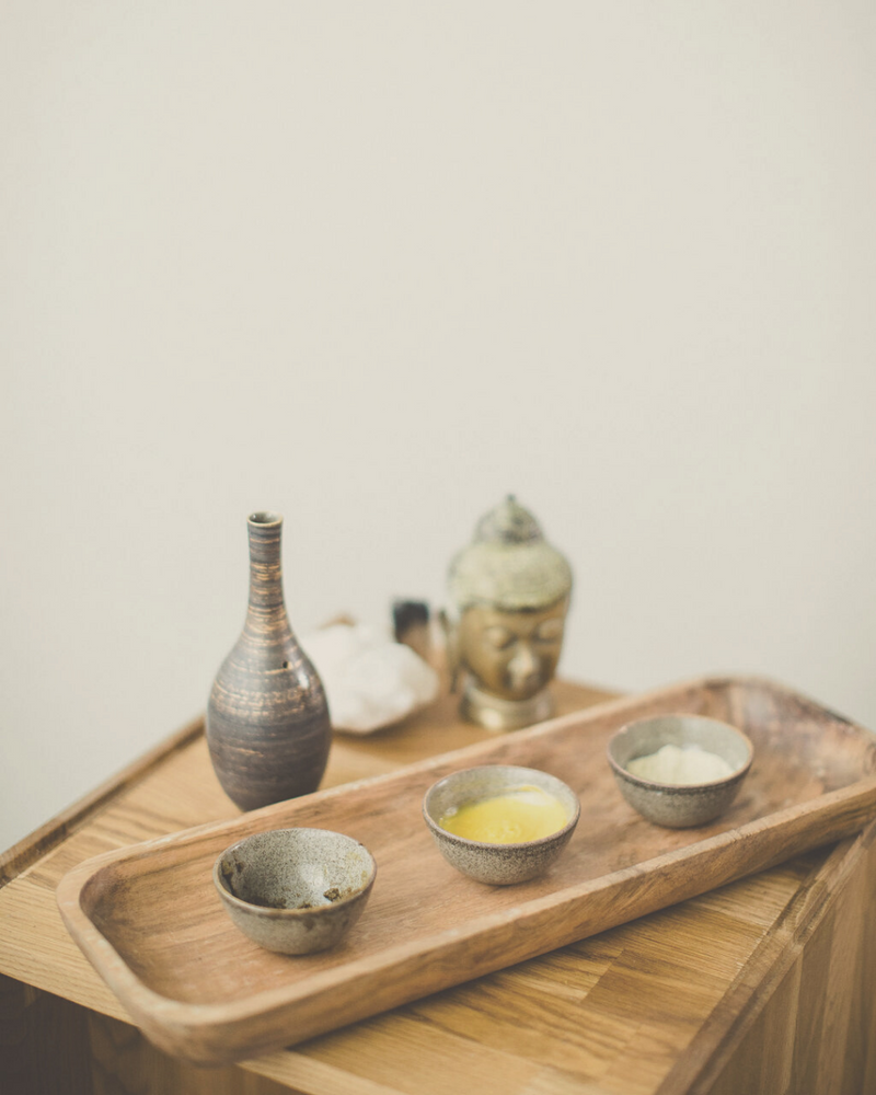 little wooden table with organic, Ayurvedic, raw skincare products in little ceramic pots with a golden Buddha statue