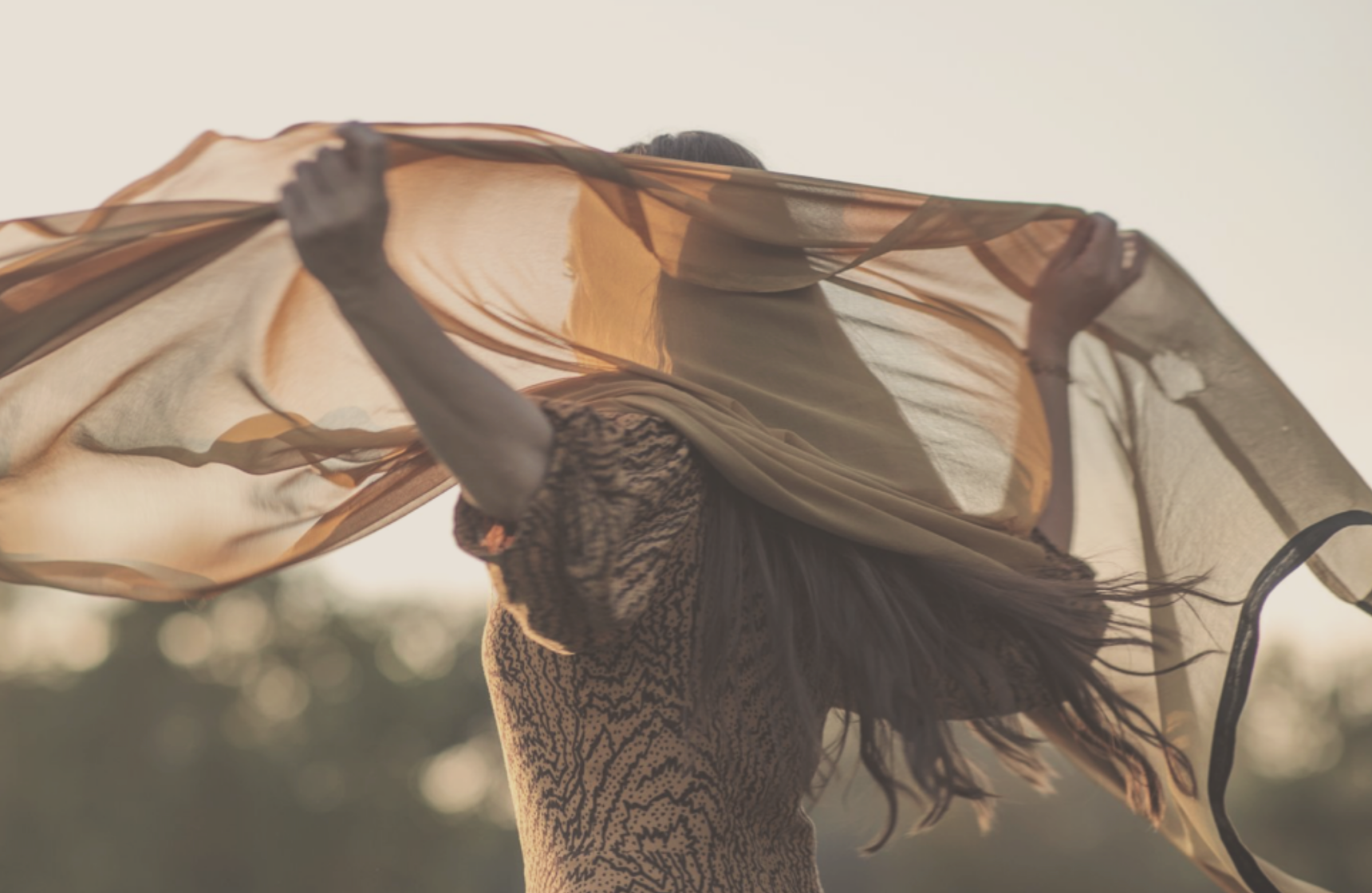 woman holding a lose scarf into the air in the late summer afternoon immersed into the golden light of the sun