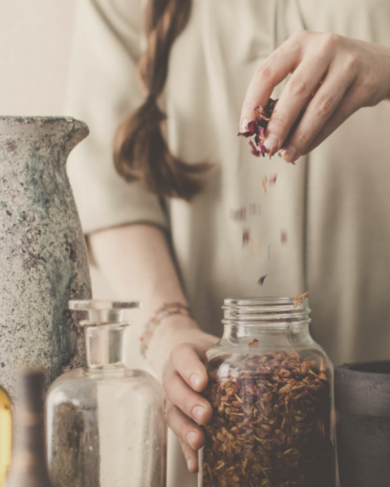 woman sprinkling Ayurvedic herbs into a glass jar