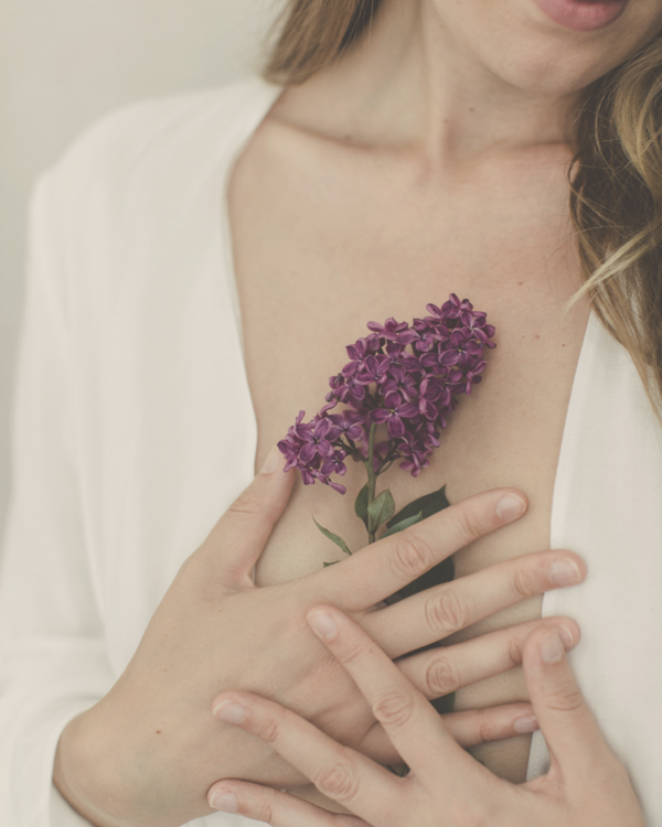 closeup of woman's  holding a purple flower close to her heart with both hands-SKIND Ayurvedic cleansing & reconnecting programme