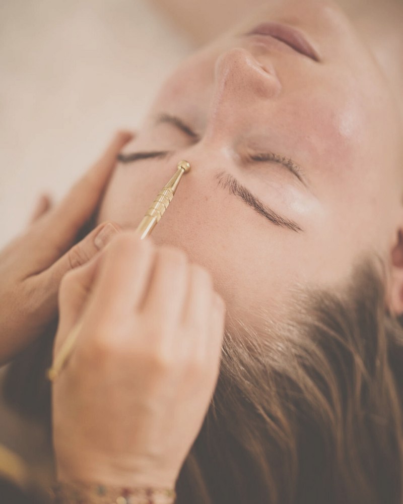woman receiving a reflexology face massage with a golden reflexology tool - stimulating the marma points ion her face
