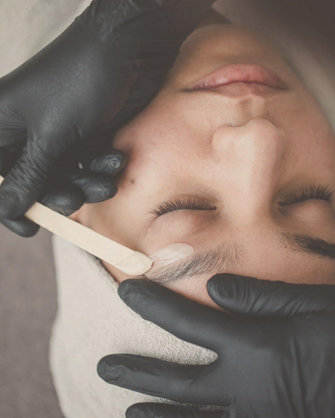 close-up of a woman's face receiving face wax hair removal to form her eyebrows 