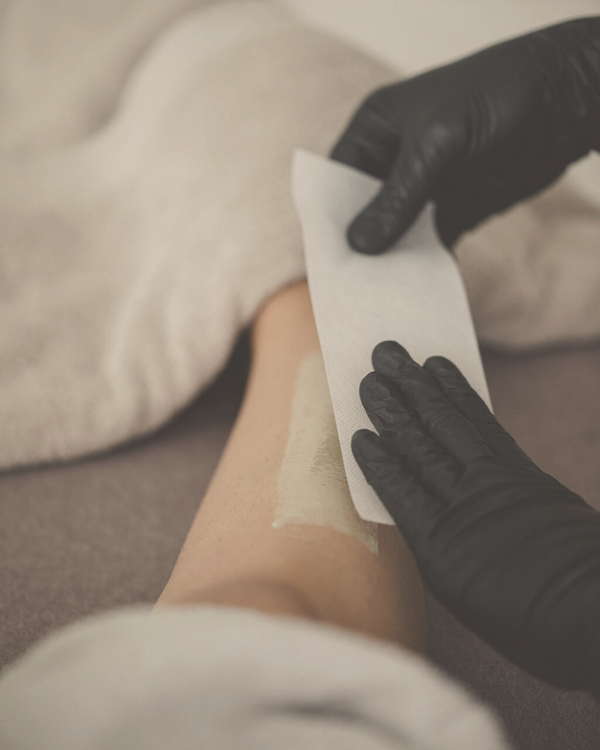 close up of a woman's leg with body wax on it and hands ready to put a sheet of paper on it to perform body wax hair removal
