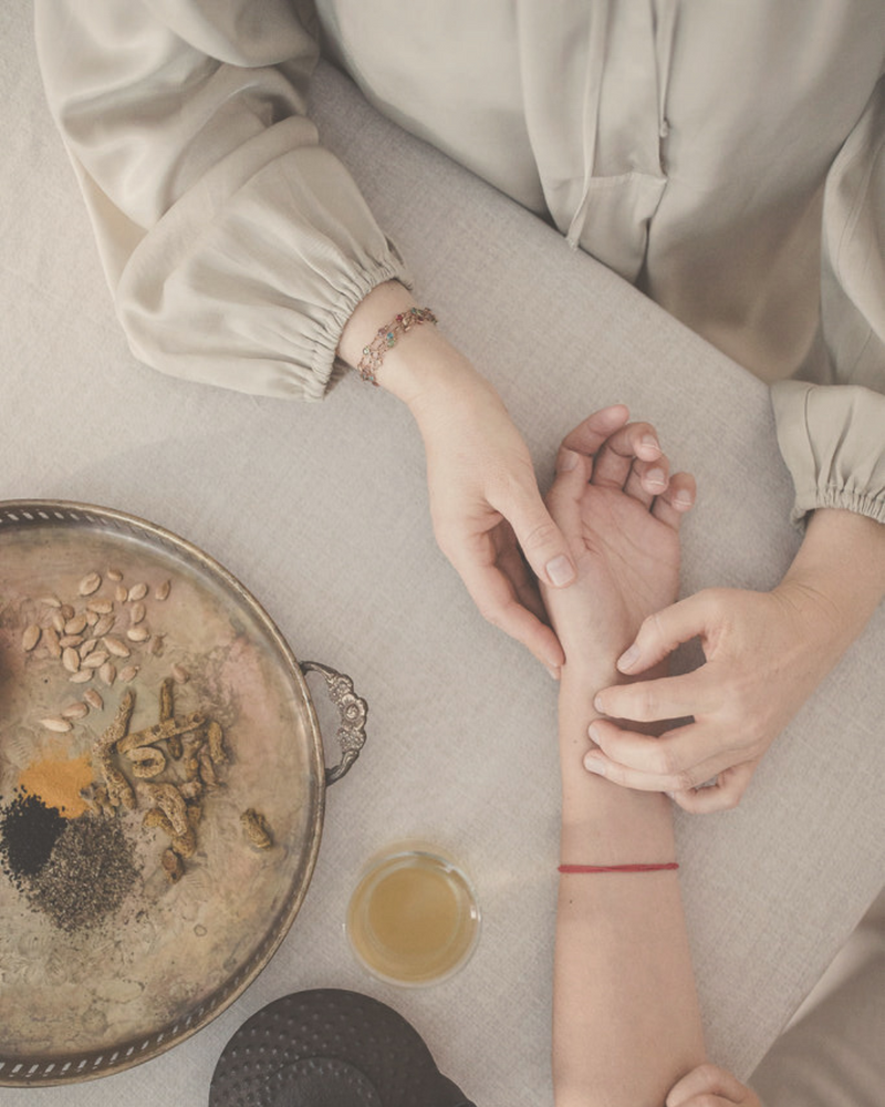 woman's hands performing pulse diagnostic on other woman's hand, ayurvedic herbs and tea